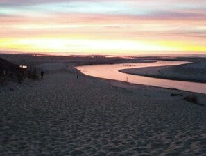 A wide river with gentle curves, surrounded by sandy terrain and a few distant structures.