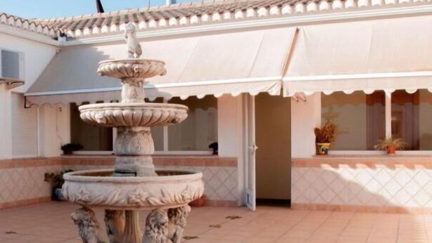 A courtyard with a multi-tiered fountain and a building with a tiled roof and white walls. - Hotel Lindaraja (Albolote)