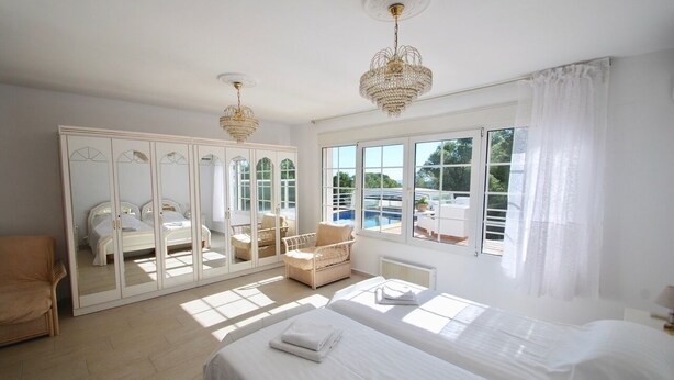 A bright bedroom with two beds, a large mirror, a chair, and a view of a pool. - The Great Luxury Villa Villa of Atenea (Cautivador)