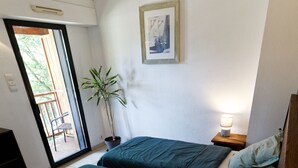 Ein Schlafzimmer mit zwei Betten, einem Blumentopf, einem Nachttisch mit Lampe und einem Fenster mit Blick ins Freie.