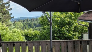 Eine Holzterrasse mit Tisch und Sonnenschirm, mit Blick auf eine bewaldete Landschaft.