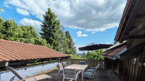 Eine Holzterrasse mit Tisch und Stühlen, mit Blick auf ein Gewässer, umgeben von Bäumen.