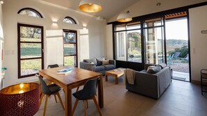 Ein geräumiger Wohnbereich mit Esstisch, Sofas und großen Fenstern mit Blick ins Freie.