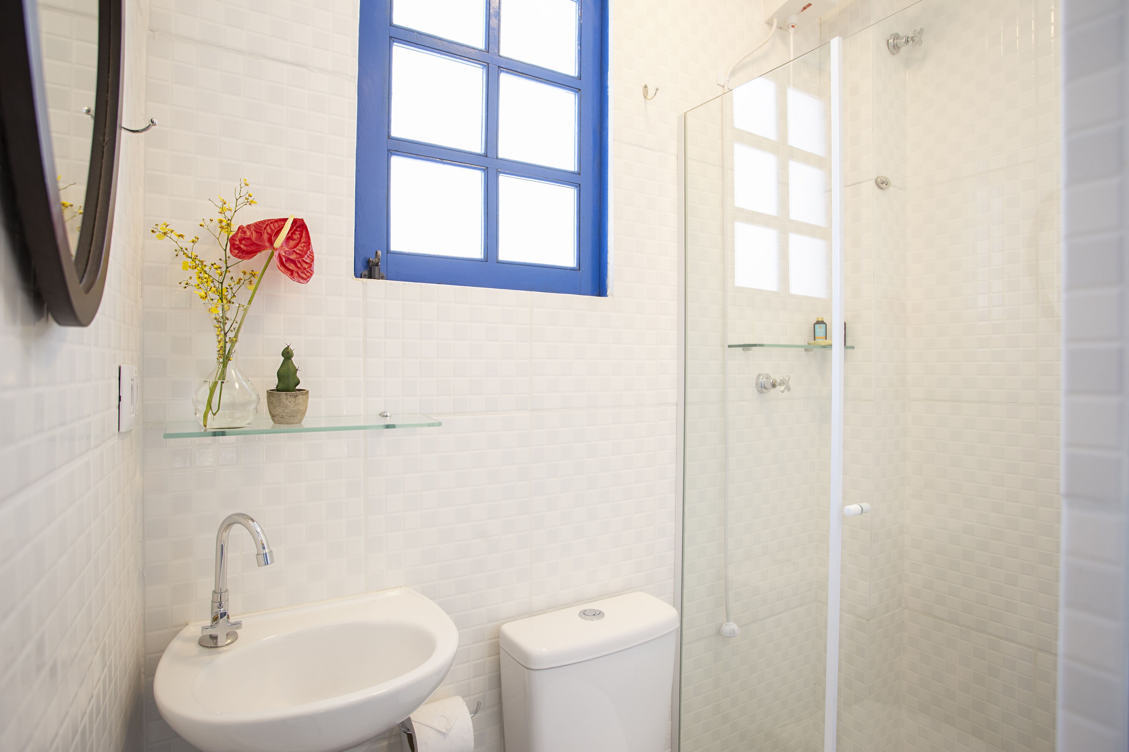 Ein Badezimmer mit einem weißen Waschbecken, einer Toilette, einer Duschkabine aus Glas und einem blau gerahmten Fenster.