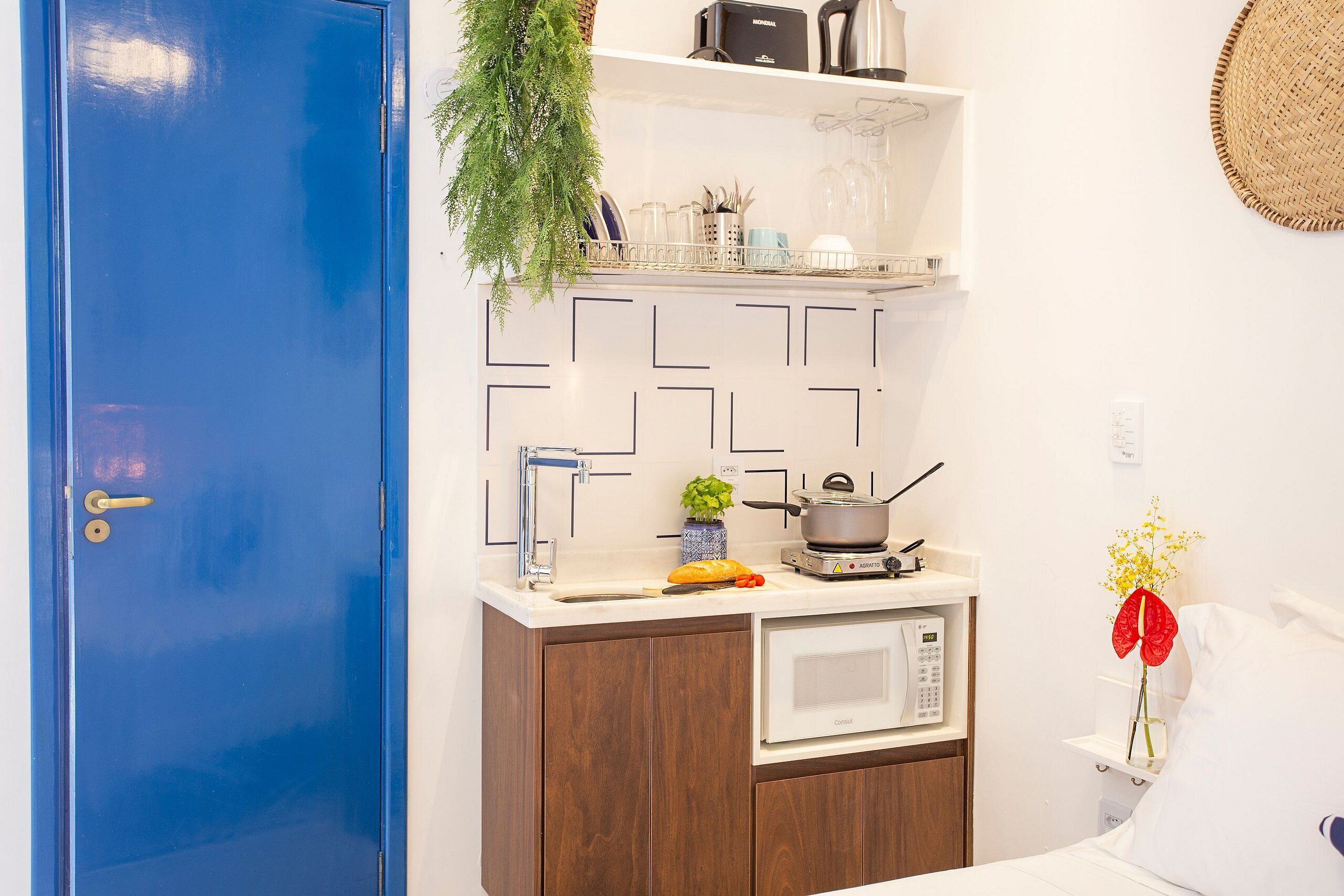 A compact kitchenette with a microwave, a small stove, and a sink. There is a plant on the countertop and a basket of bread on the counter.