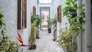 A narrow stone pathway flanked by white walls and wooden shutters, leading to a covered area with steps. - Vila Grega (São Paulo)