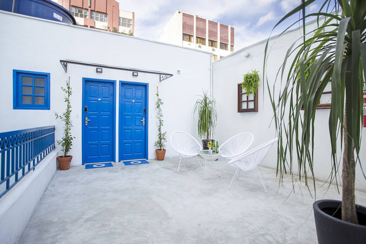 Une cour avec deux portes bleues, des chaises blanches et des plantes en pot.