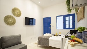 A modern bedroom with a grey sofa, a bed with a grey and white bedspread, a blue door, and a flat-screen TV on the wall. - Vila Grega (São Paulo)