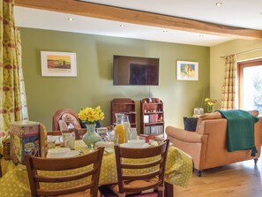 A dining area with a table set for two, a television mounted on the wall, and a bookshelf.