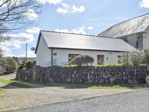 A white building with a sloped roof, a stone wall in front, and a gravel driveway.