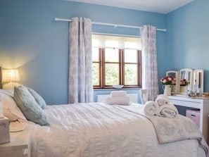 A bedroom with a bed, a desk, a chair, a lamp, and a window with curtains.