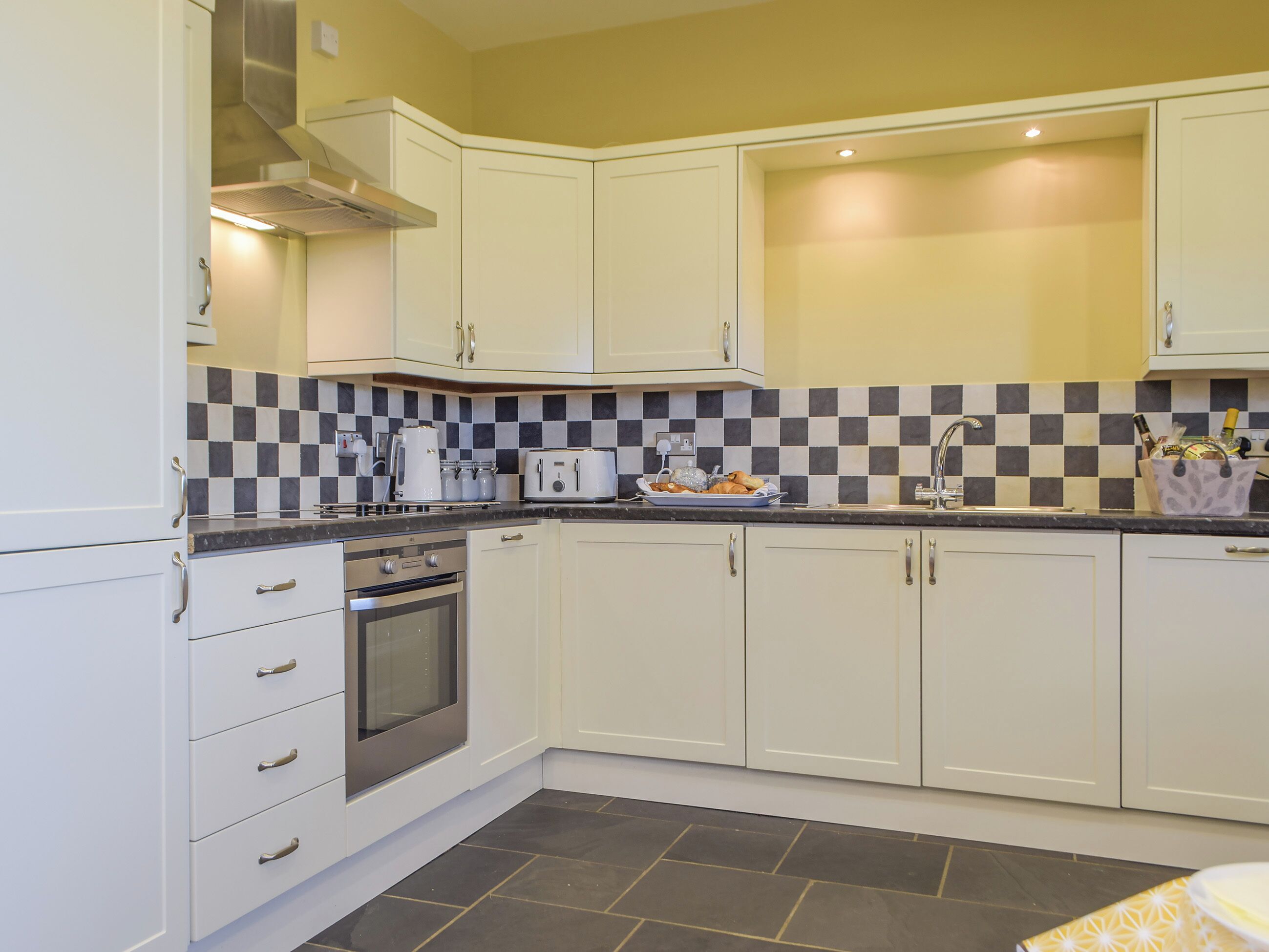 A modern kitchen with white cabinets, a stainless steel oven, a checkered backsplash, and a sink with a faucet.