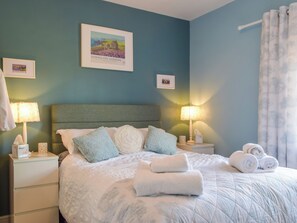 Un lit bien fait, avec des oreillers et des serviettes enroulées, une table de chevet avec une lampe et un tableau encadré au mur.