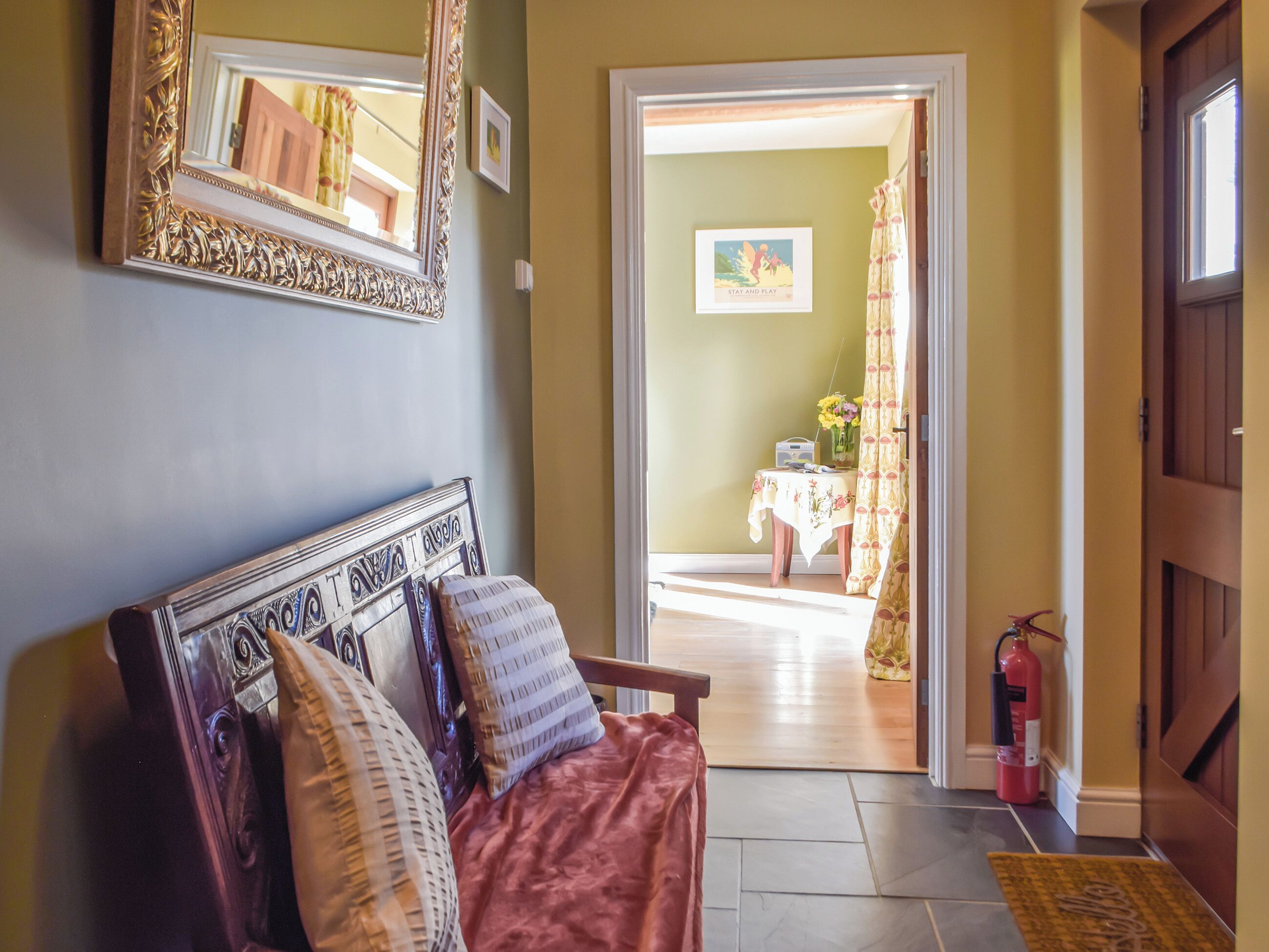 A room with a sofa, a mirror, a door leading to another room, and a fire extinguisher.