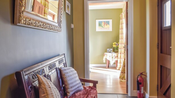 A room with a sofa, a mirror, a door leading to another room, and a fire extinguisher.