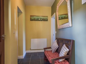 Un couloir avec un radiateur, un banc agrémenté de coussins et un tableau accroché au mur.