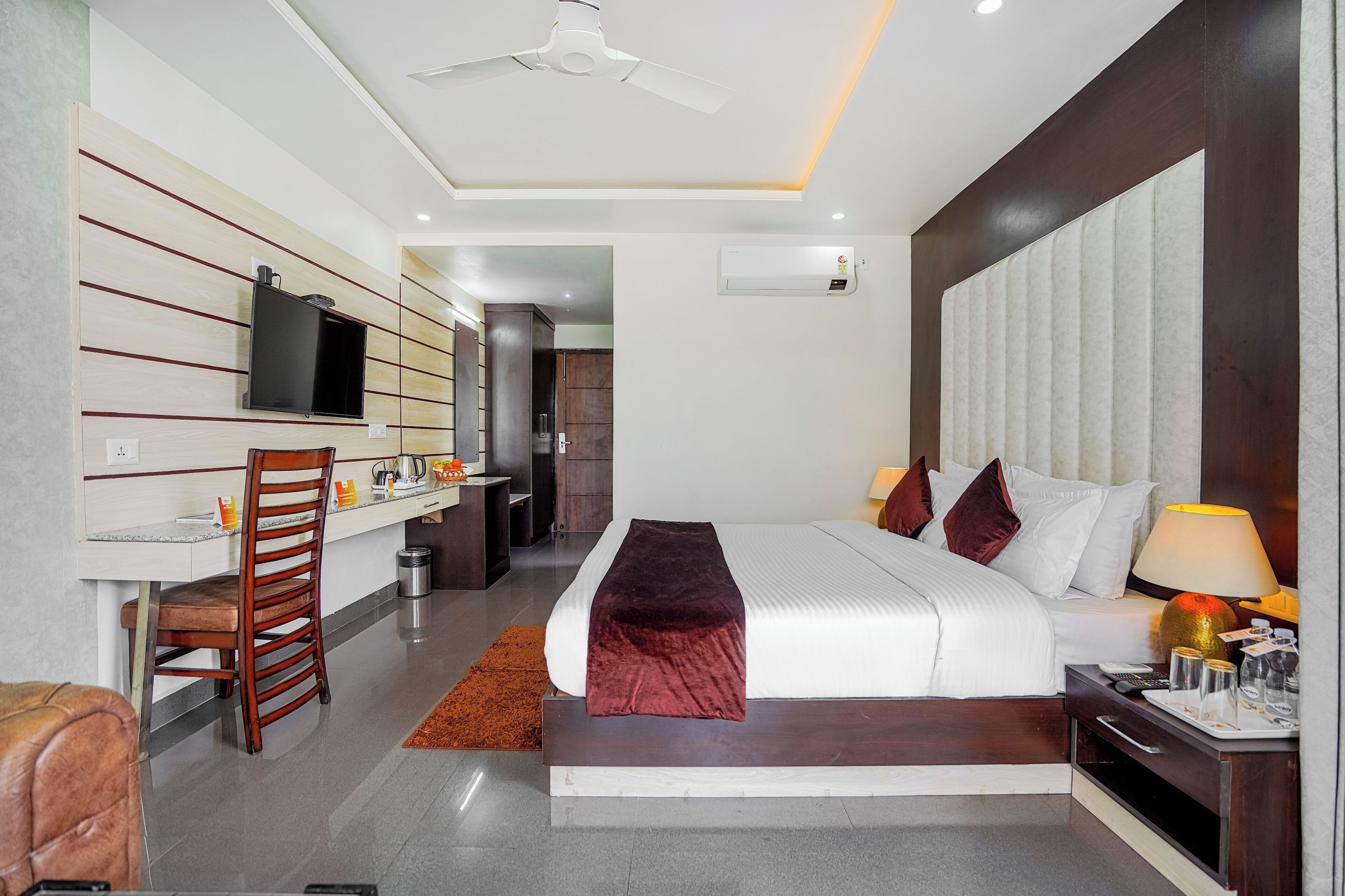 A modern hotel room with a large bed, a desk, a television, and a ceiling fan.