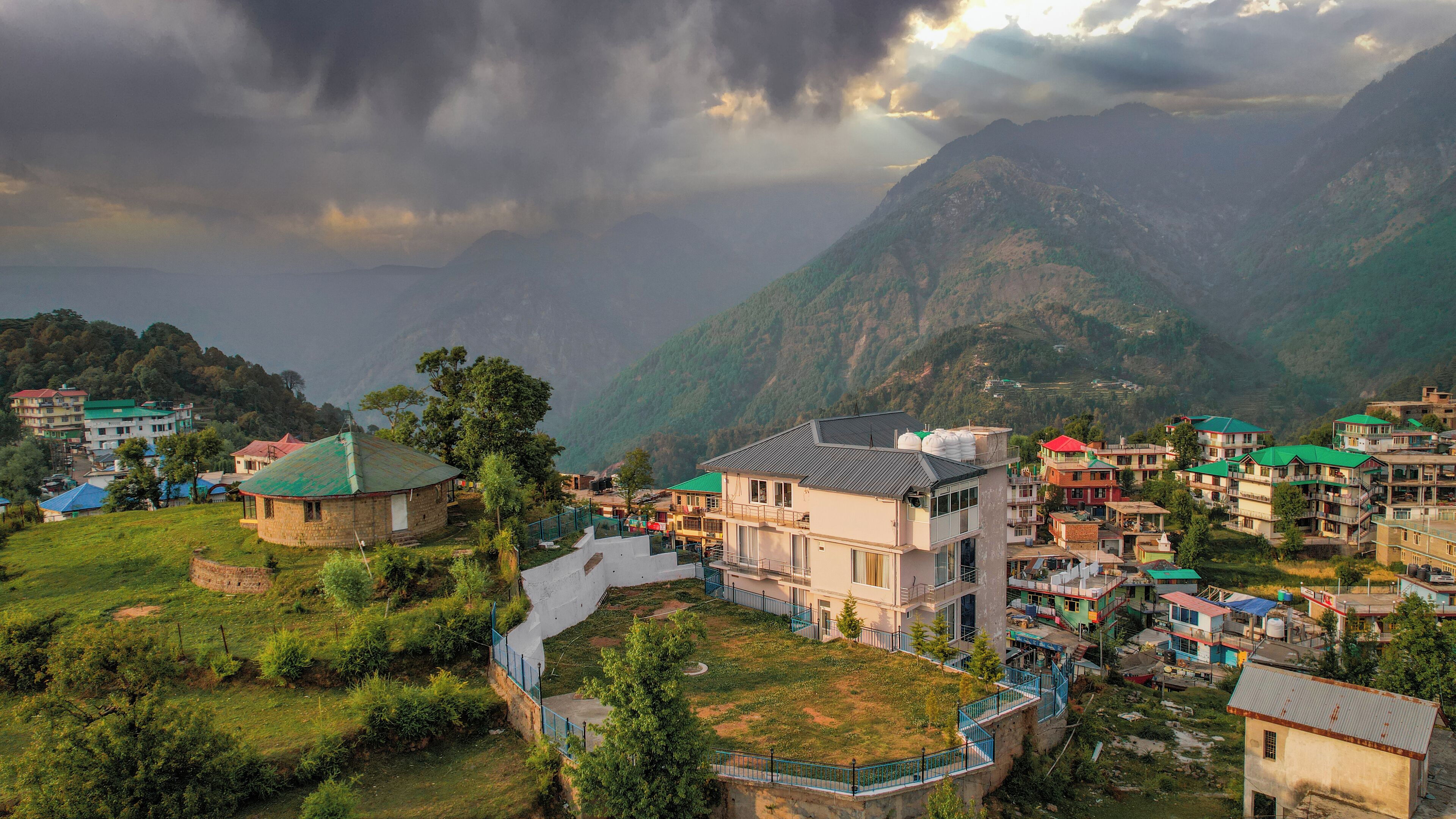 A hillside village with traditional houses, a central building with a flat roof, and a view of the surrounding mountains.