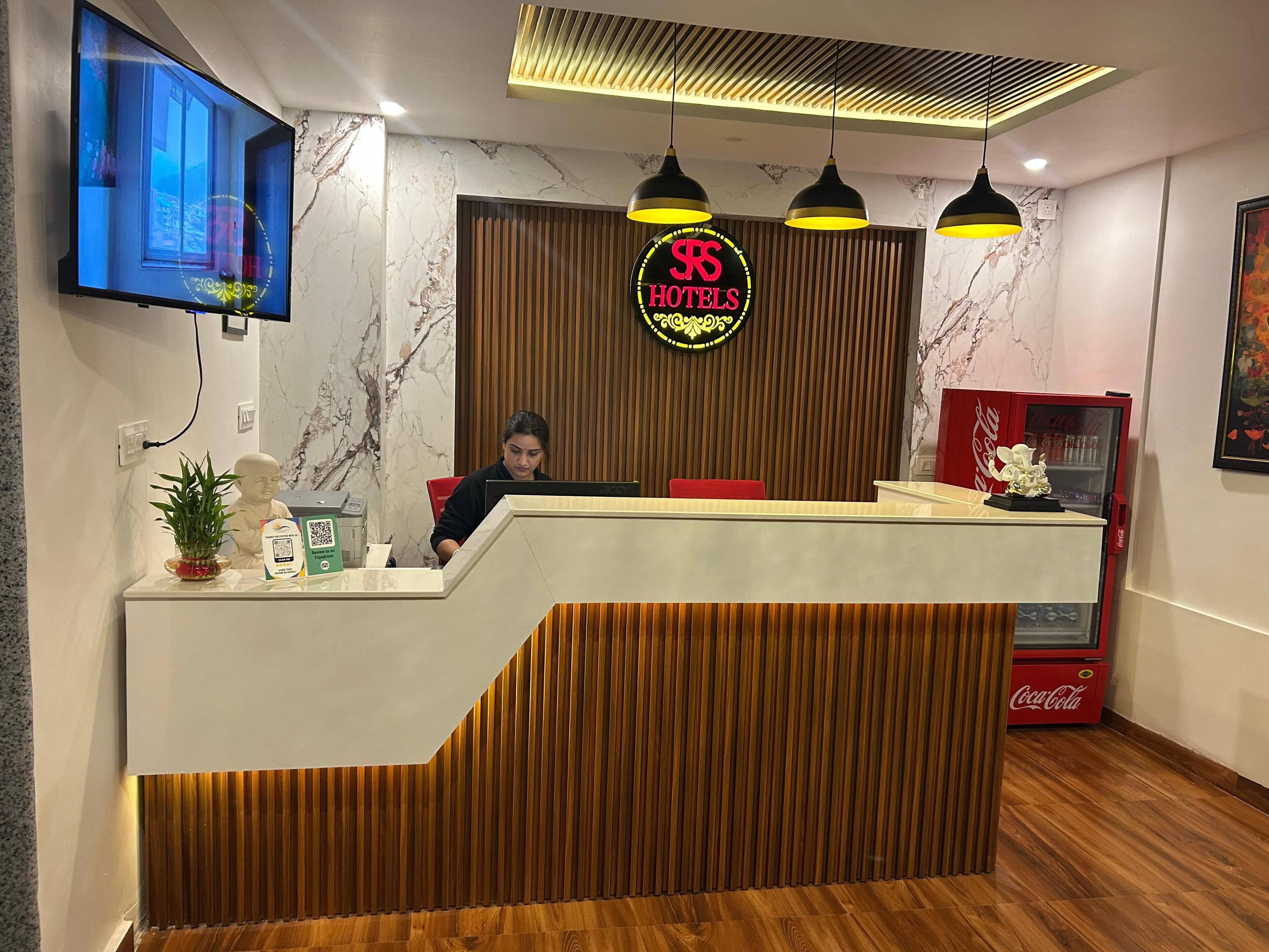 A hotel reception desk with a modern design, a digital screen, a wooden panel wall, and a Coca-Cola refrigerator.
