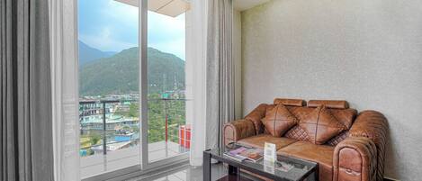 A modern living room with a leather sofa, a glass coffee table, and a large window offering a view of a mountainous landscape.