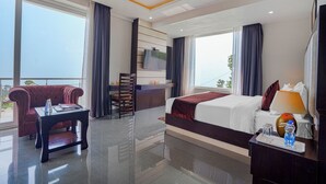 Habitación de hotel con cama, escritorio, silla, televisión montada en la pared y balcón con cortinas.