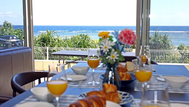 A breakfast table with croissants, orange juice, and a vase of flowers, overlooking a scenic ocean view. - Ocean Villa Tokunoshima (Tokunoshima)