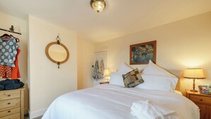 A neatly made bed with white linens, a round mirror, and a painting on the wall.