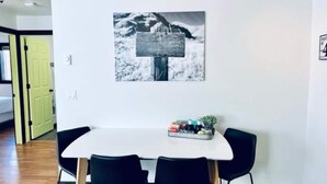 A dining area with a white table, black chairs, and a black and white photograph on the wall.