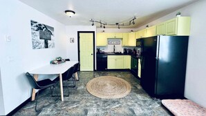 A compact kitchen with a dining area, a black refrigerator, and a 'let's eat' sign on the wall.
