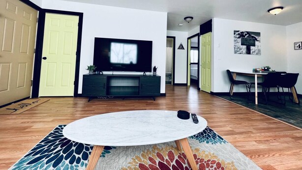 A modern living room with a flat-screen TV, a round coffee table, and a dining area with a table and chairs.