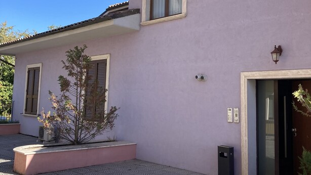 Un edificio con fachada rosa, un patio empedrado y una puerta con una pequeña planta a un lado.