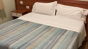 Una cama bien hecha con una colcha a rayas y almohadas blancas, un cabecero de madera y una mesita de noche con una lámpara.