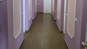 Un pasillo con paredes moradas y suelo de madera, que conduce a una puerta blanca al final.