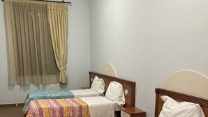 Una habitación de hotel con dos camas individuales, una mesita de noche de madera, una mesa y una ventana con cortinas.