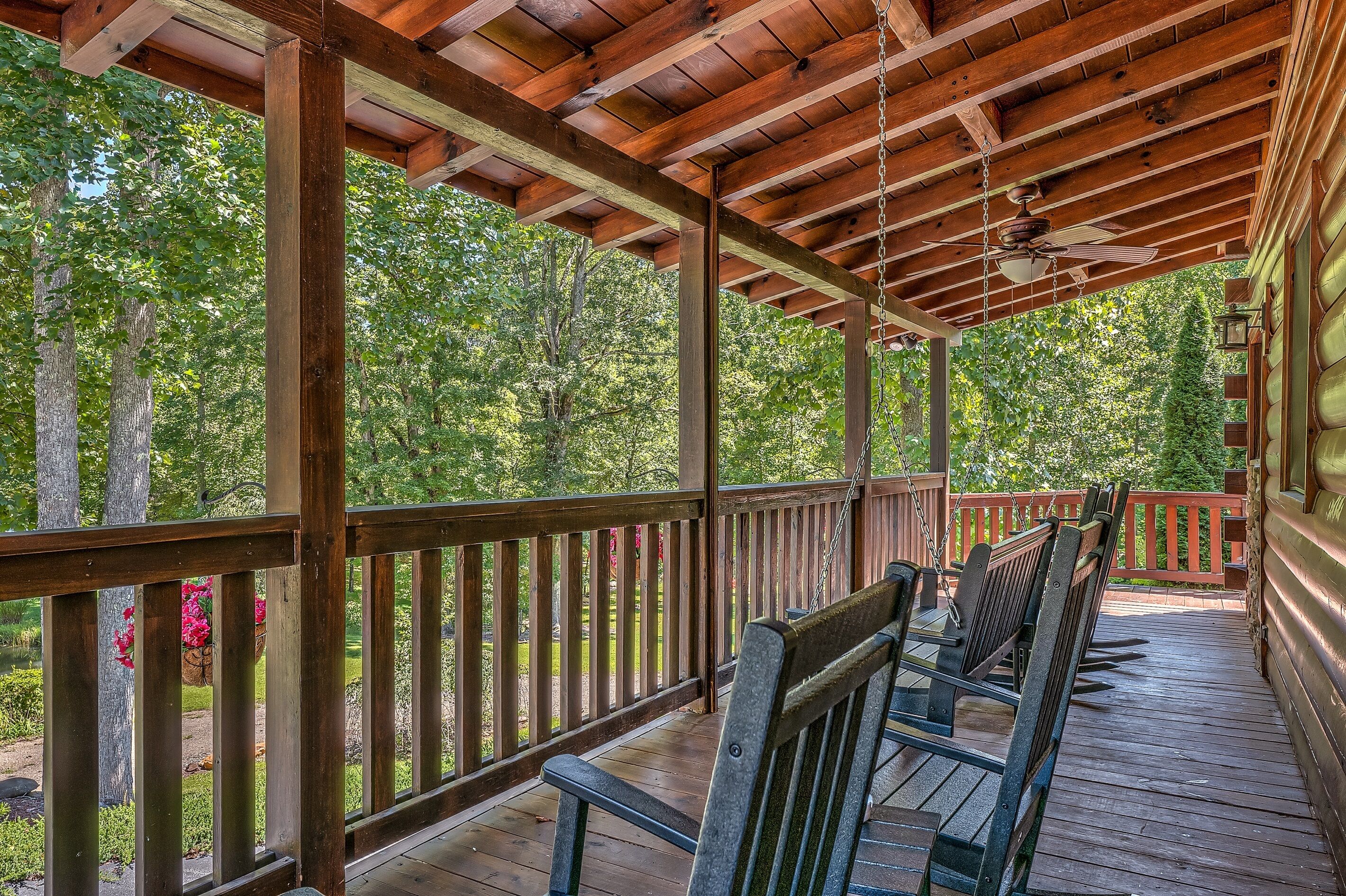A wooden deck with a ceiling fan, wooden railings, and a view of a wooded area.