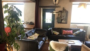 A cozy living room with a black leather sofa, a green armchair, and a dining table with a metal tray.