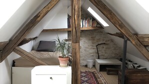 A cozy attic bedroom with a sloped ceiling, a white bed, a small white dresser, a green rug, and a potted plant.