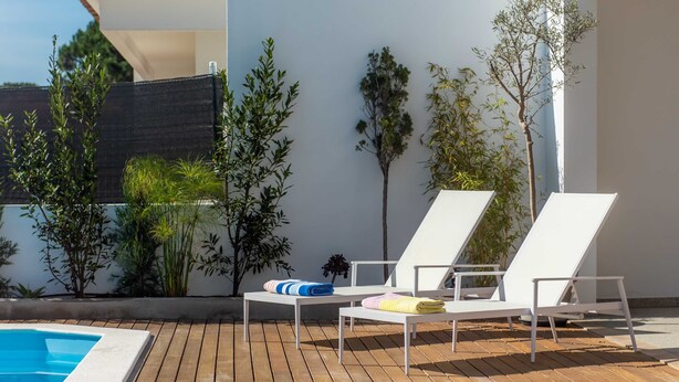 A poolside area with wooden decking, white lounge chairs, and a small table with towels. - LV Premier LA2 Pool AC Garden sea View  (Sesimbra)