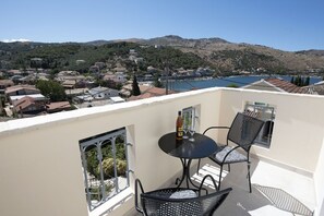 A balcony with a table and chairs, overlooking a hillside with houses and a body of water.