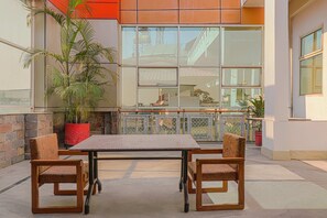Un espace extérieur aménagé avec une table et des chaises, des plantes en pot et une vue sur un bâtiment doté de grandes fenêtres.