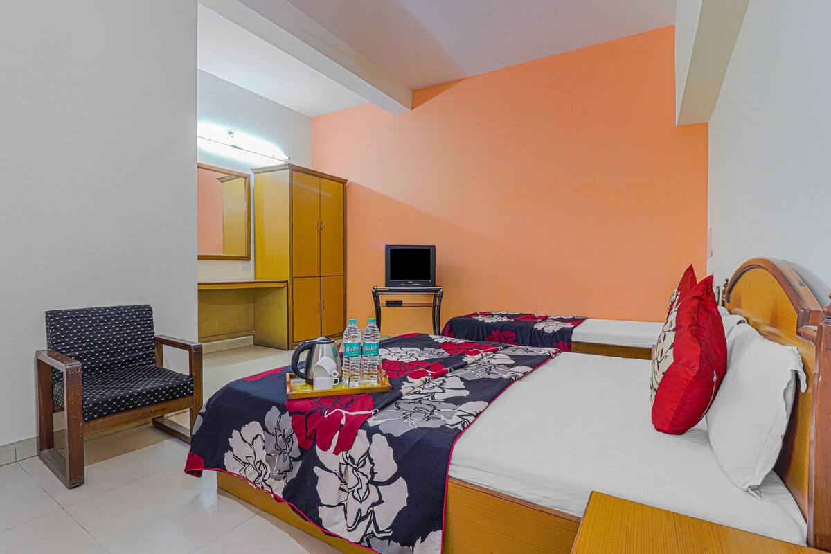 A hotel room with a bed, a chair, a TV, and a minibar.