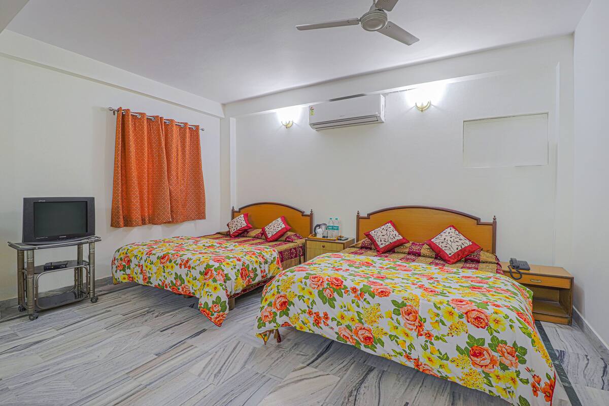 A hotel room with two beds, a TV on a cart, an air conditioner, and a ceiling fan.