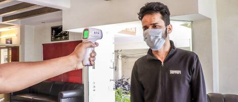 Une personne se fait prendre la température à l’aide d’un thermomètre infrarouge portatif dans une pièce dont le plafond est en bois, qui contient un canapé et dont on aperçoit une porte au fond.