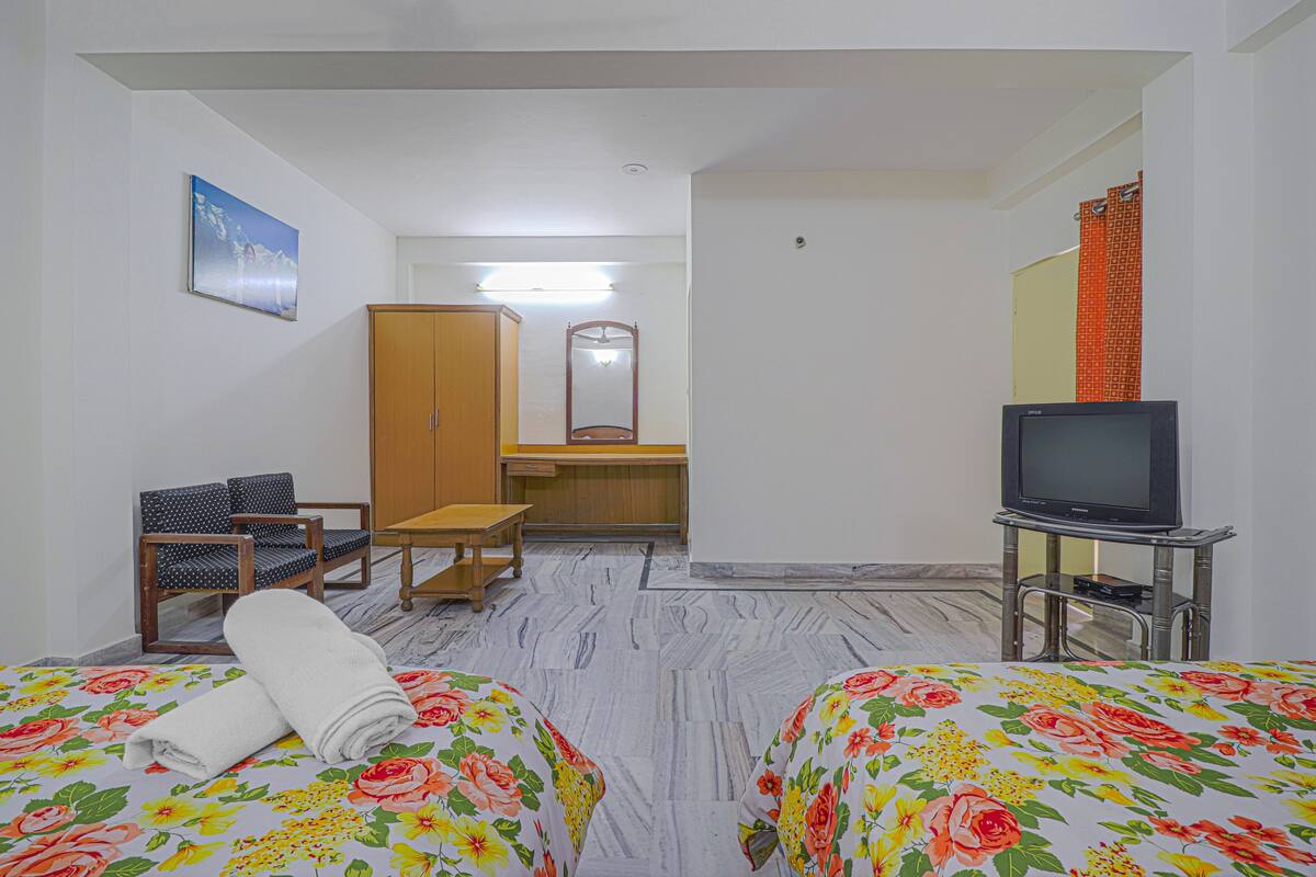 A hotel room with two beds, a television, a desk, a mirror, and a wardrobe.