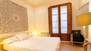 A neatly arranged bedroom with a large bed, a decorative wall piece, a window with wooden shutters, and a chair with a cushion. - Lovely 2-bed Apartment in Rawalpindi (Rawalpindi)