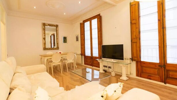 A living room with a white sofa, a glass coffee table, a TV on a stand, and a dining area with chairs and a table. - Lovely 2-bed Apartment in Rawalpindi (Rawalpindi)