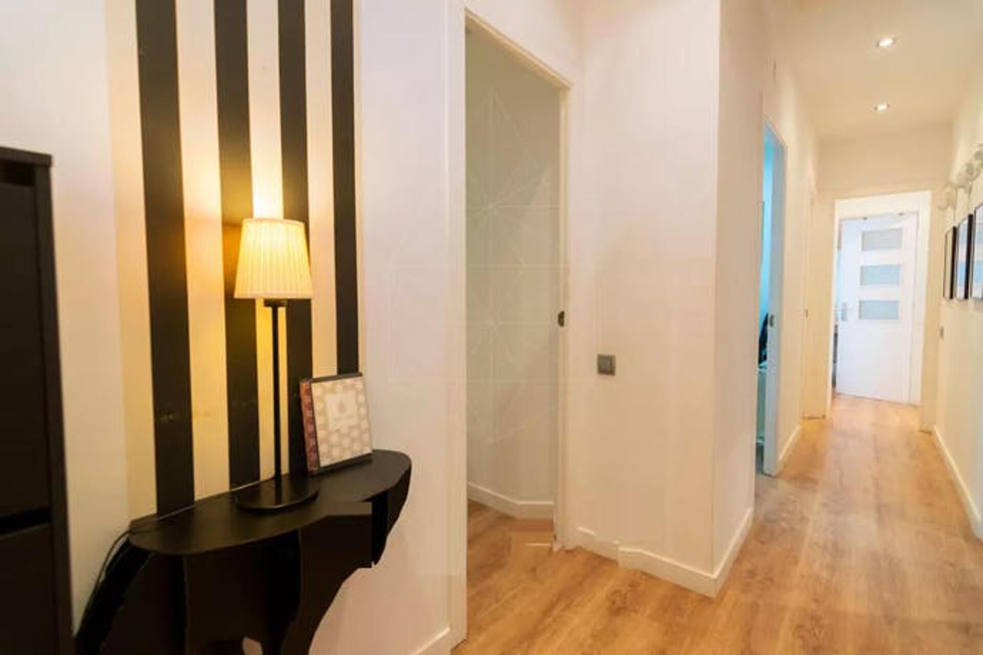 A hallway with a black console table, a lamp, and a door leading to another room.