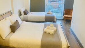 Ein Hotelzimmer mit zwei Betten, einem Sessel und einem großen Fenster mit Jalousien.