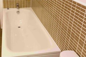 A bathroom with a white bathtub, a toilet, and a tiled wall.