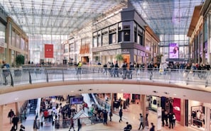 A multi-level shopping mall with a glass ceiling, escalators, and various retail stores.